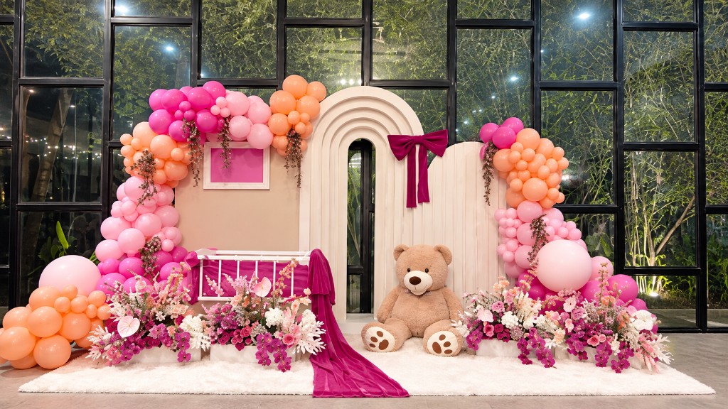 BBPremium balloon backdrop with pink and peach garlands, a baby crib, florals and a teddy bear.