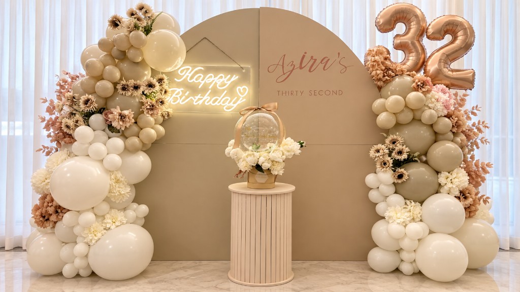 Two-panel balloon backdrop with Happy Birthday neon, floral balloon garlands and a gift-box pedestal.